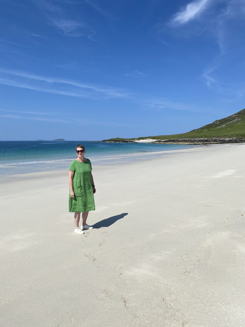 Jennifer Ellis standing on a white sand beach under a blue sky, wearing a green linen dress